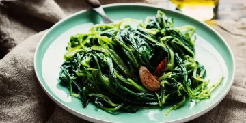 su un tavolo di legno piatto blu con la cicoria ripassata e accanto una bottiglia di olio d'oliva