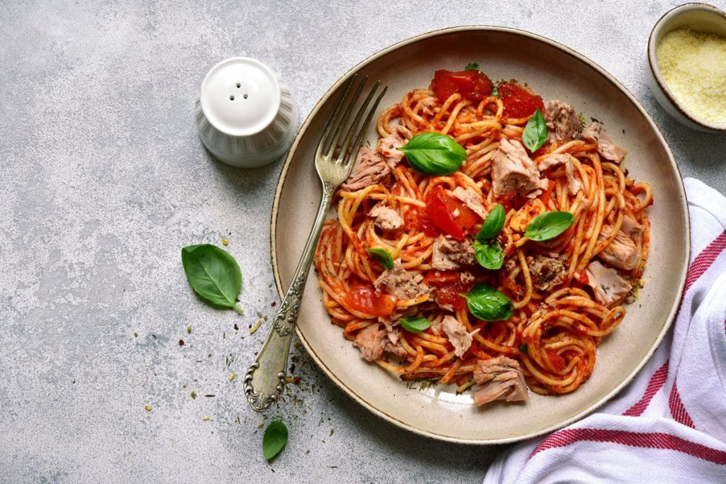 in primo piano su un piatto fondo degli spaghetti al tonno con pomodoro e qualche foglia di basilico