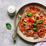 in primo piano su un piatto fondo degli spaghetti al tonno con pomodoro e qualche foglia di basilico