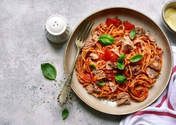 in primo piano su un piatto fondo degli spaghetti al tonno con pomodoro e qualche foglia di basilico
