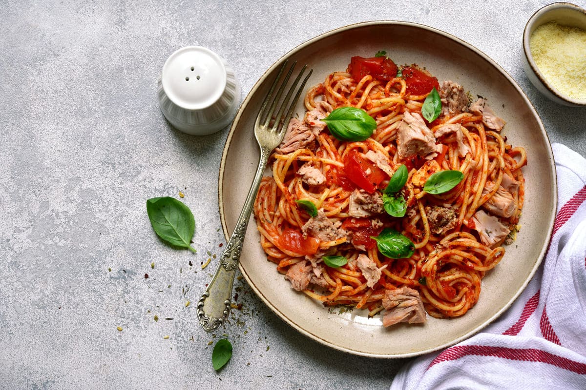 in primo piano su un piatto fondo degli spaghetti al tonno con pomodoro e qualche foglia di basilico