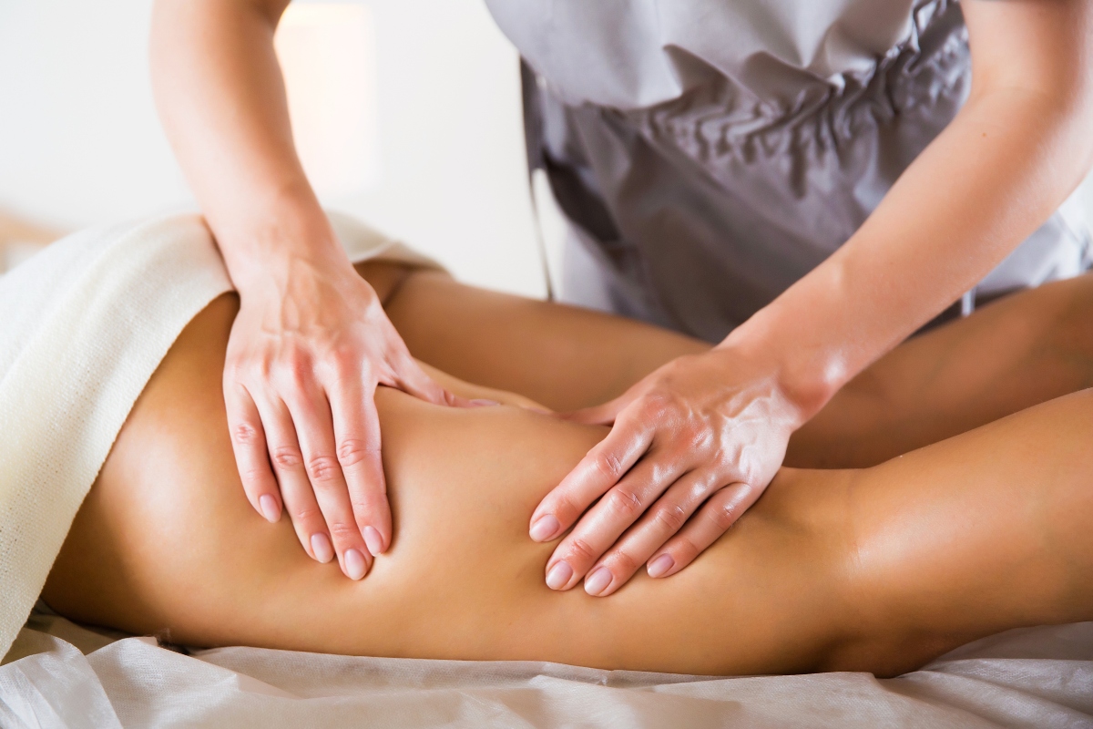 Primo piano sulle gambe di una donna durante una seduta di linfodrenaggio. Le mani dell'operatrice eseguono delicati movimenti manuali sulla coscia.