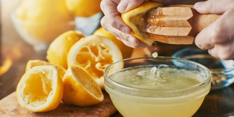 primo piano di mani che spremono limoni per bere acqua e limone al mattino con bucce di limoni