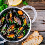 Cozze alla marinara: ricetta facile e veloce in padella 1 su tavolo di legno, padella per sauté con cozze alla marinara, attorno prezzemolo e 2 bruschette