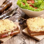 su tavolo di legno due toast croque monsieur accanto a una scodella di insalata e un macina pepe