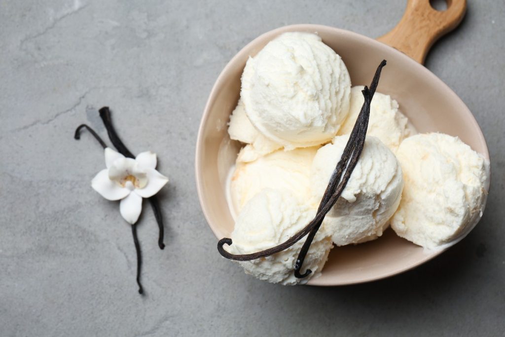 su tavolo di marmo grigio, ciottola con 3 palline di gelato alla vaniglia e bacche di vaniglia. Accanto bacche di vaniglia con il fiore