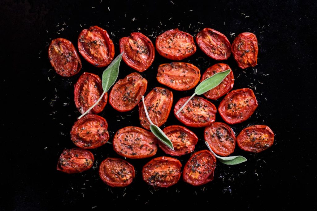 Pomodorini confit: la ricetta da fare a casa 4 su sfondo nero, primo piano di pomodorini confit con foglie di alloro