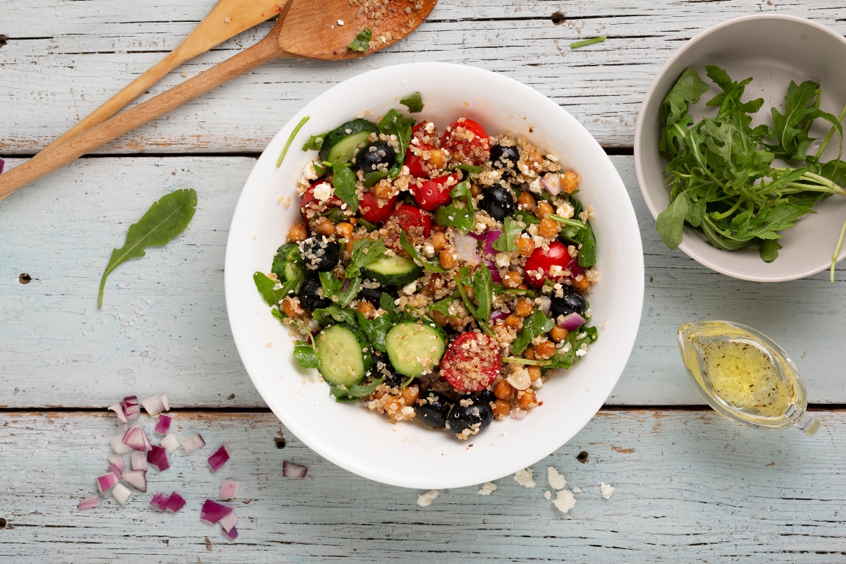 su tavolo di legno bianco, ciotola con una delle migliori ricette con quinoa: insalata di quinoa con pomodori, zucchine e olive