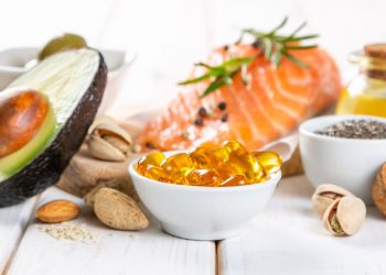 alimenti ricchi di omega-3: su base chiara mezzo avocado, un trancio di salmone e ciotole con frutta secca