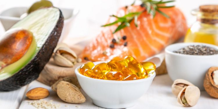 alimenti ricchi di omega-3: su base chiara mezzo avocado, un trancio di salmone e ciotole con frutta secca