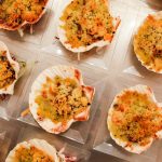 Capesante gratinate al forno, ricetta e video ricetta di un secondo piatto delizioso 1 su tavolo di legno chiaro piatti trasparenti con capesante gratinate