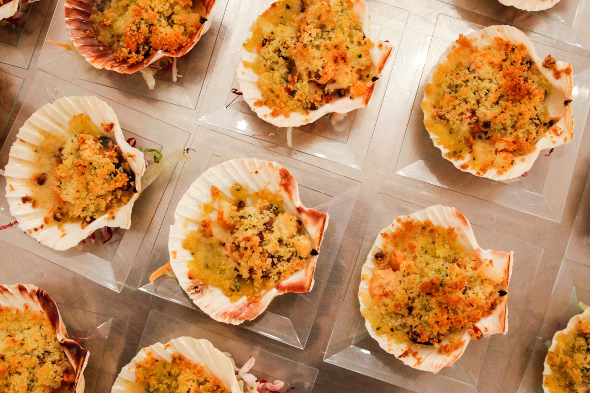 su tavolo di legno chiaro piatti trasparenti con capesante gratinate