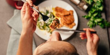 vediamo di spalle una persona che sta mangiando da un piatto davanti a sé