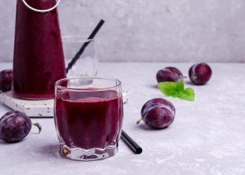 lassativi naturali: prugne sparse e un bicchiere pieno di succo di prugne