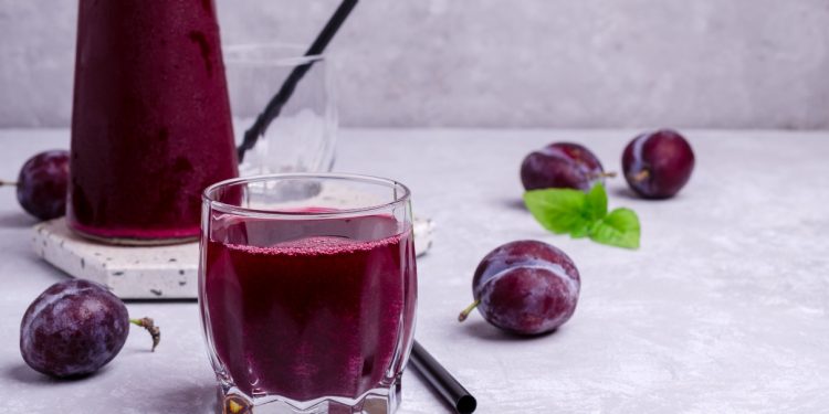 lassativi naturali: prugne sparse e un bicchiere pieno di succo di prugne