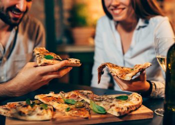 un uomo e una donna che tengono in mano una fetta di pizza
