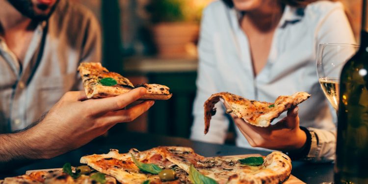 un uomo e una donna che tengono in mano una fetta di pizza