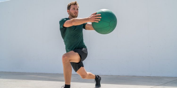 Uomo in allenamento outdoor esegue un affondo laterale con la palla medica