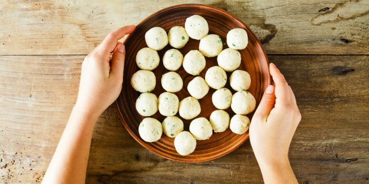 su tavolo di legno. mani di una donna che fa vedere una ciottola con diverse polpette di ricotta prima di infornarle