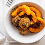 Polpette di zucca, la ricetta al forno facile e gustosa 1 In primo piano su un piatto fondo bianco ci sono delle polpette di zucca croccanti e della zucca cotta al forno.