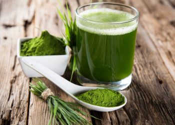spirulina: fa dimagrire? su un tavolo un bicchiere con spirulina diluita e un cucchiaio bianco con della polvere di spirulina