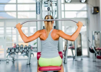 donna di spalle in palestra seduta su una macchina per esercizi dorsali