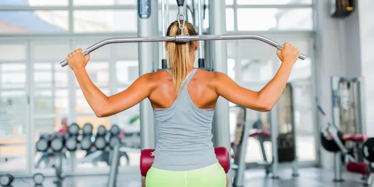 donna di spalle in palestra seduta su una macchina per esercizi dorsali
