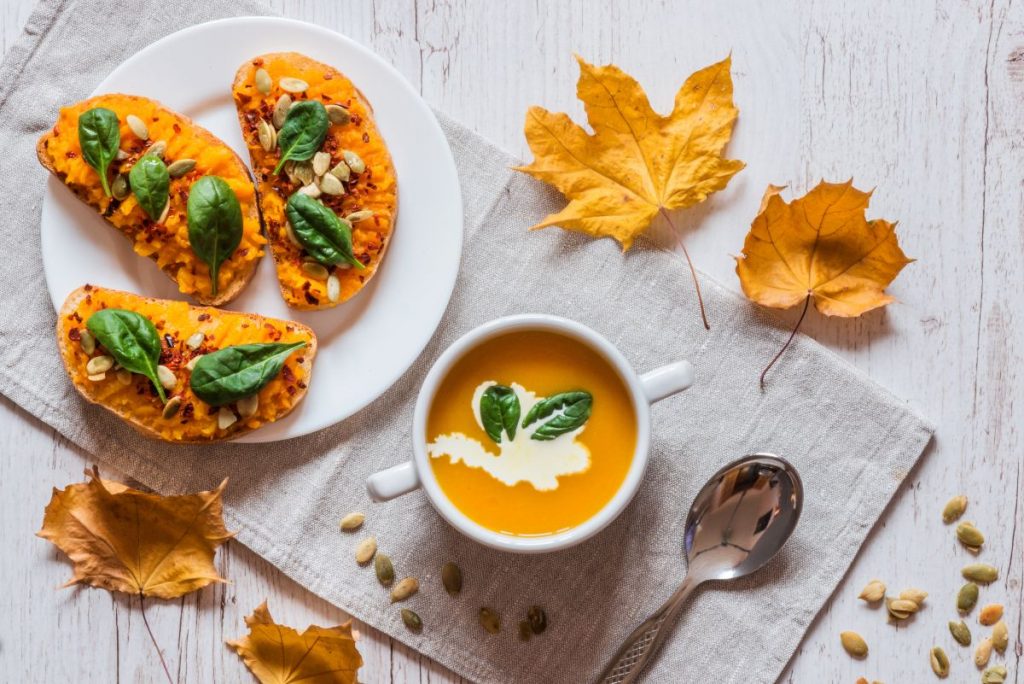 su un tavolo un piatto con bruschette con la zucca e una tazza con una vellutata di zucca