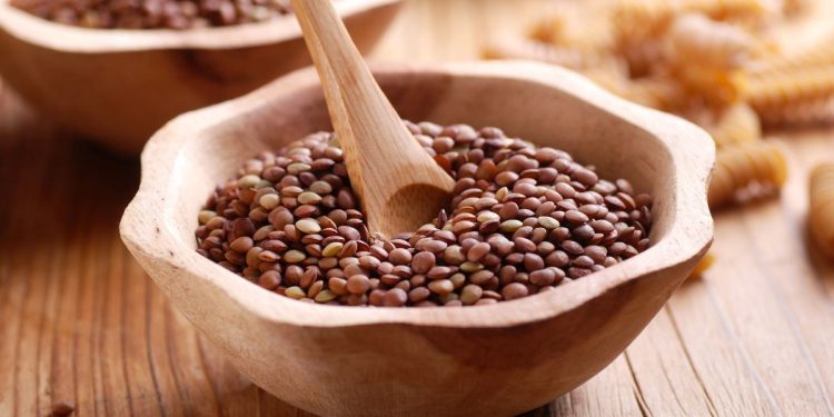 ciotola di legno con lenticchie secche e un cucchiano, su base di legno