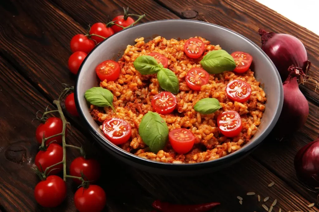 Risotto al pomodoro: la ricetta per farlo cremoso e gustoso 3 padella tonda con risotto al pomodoro e foglie di basilico, pomodorini e cipolle rosse intorno