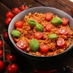 padella tonda con risotto al pomodoro e foglie di basilico, pomodorini e cipolle rosse intorno