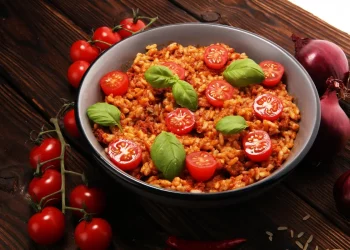 padella tonda con risotto al pomodoro e foglie di basilico, pomodorini e cipolle rosse intorno