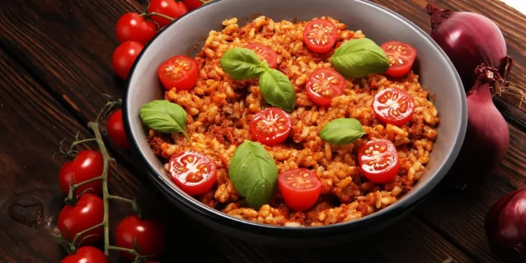 padella tonda con risotto al pomodoro e foglie di basilico, pomodorini e cipolle rosse intorno