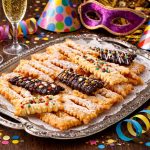 vassoio in argento con sopra le frappe al forno intorno bicchieri e mascherine e stelle filanti