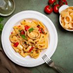 Calamarata napoletana: la ricetta originale e facile 1 In primo piano su uno sfondo scuro, c'è un piatto di calamarata con pomodorini freschi. Sullo sfondo c'è la pasta con i pomodori.