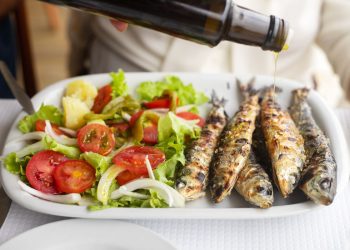 Un piatto con insalata e delle sardine condite con olio di oliva