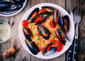 su un piano di cucina primo piano di un piatto di spaghetti con le cozze, un bicchiere di vino, una forchetta e un coltello e un tappo di bottiglia