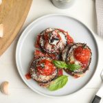 Melanzane alla parmigiana light: la ricetta al forno facile e gustosa 1 In primo piano su un piatto fondo bianco ci sono delle porzioni di melanzane alla parmigiana decorate con delle foglie di basilico.
