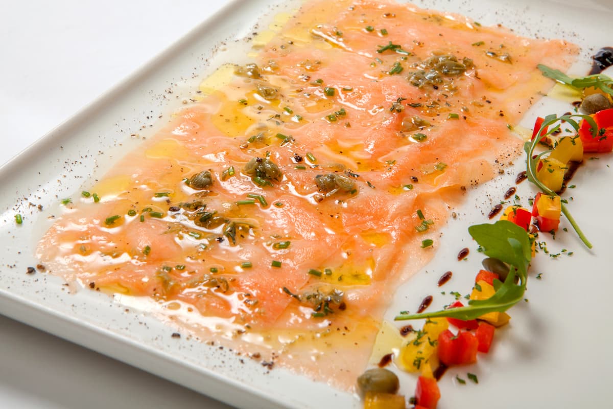 piatto rettangolare con carpaccio di salmone marinato decorato con capperi e verdure tagliate