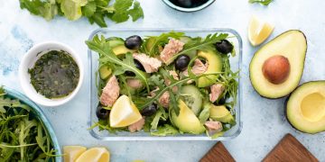 lunch box con insalata e tonno in scatola con attorno avocado, olive, limone