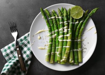 cosa mangio stasera: su sfondo nero piatto bianco con asparagi in padella con burro e Parmigiano, sulla sinistra tovagliolo a quadretti bianco e verde