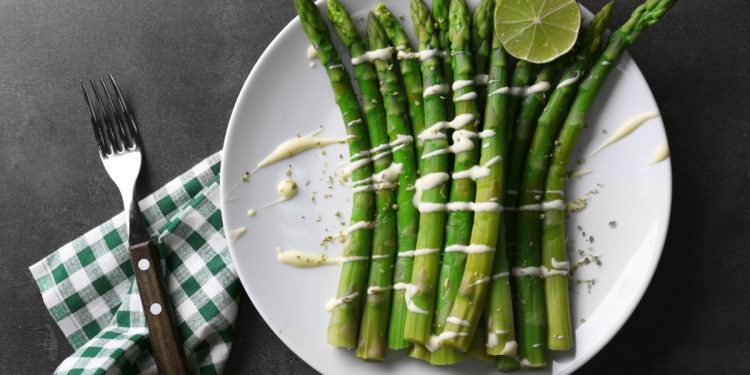 cosa mangio stasera: su sfondo nero piatto bianco con asparagi in padella con burro e Parmigiano, sulla sinistra tovagliolo a quadretti bianco e verde