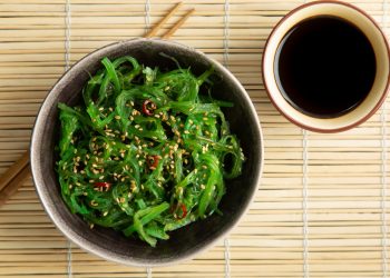 sottopiatti di bambù con una ciottola piena di alga wakame con bacchette giapponesi e salsa di soia