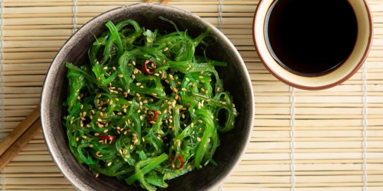 sottopiatti di bambù con una ciottola piena di alga wakame con bacchette giapponesi e salsa di soia
