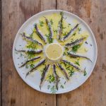 su tavolo di legno, piatto bianco con alici marinate, olio Evo e una fetta di limone al centro