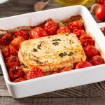 su tavolo di legno, piatto da forno bianco con feta al forno e pomodorini