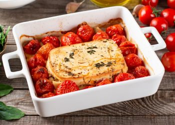 su tavolo di legno, piatto da forno bianco con feta al forno e pomodorini