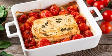 su tavolo di legno, piatto da forno bianco con feta al forno e pomodorini