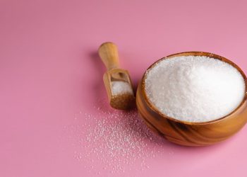 su sfondo rosa una ciotola di legno che contiene il maltitolo con accanto un cucchiaio di legno
