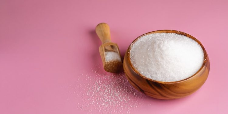 su sfondo rosa una ciotola di legno che contiene il maltitolo con accanto un cucchiaio di legno